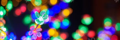 Preview: Multicolored garland flower against background of multicolored lights on Christmas night