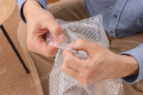 Preview: Senior man popping bubble wrap at home, closeup. Stress relief