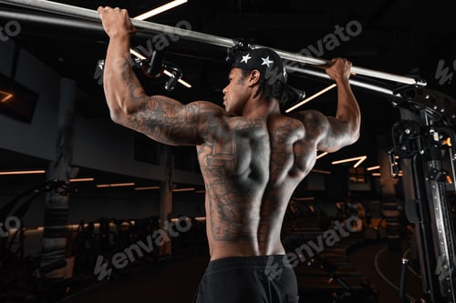 Preview: Strong and muscular dark skin man trains on modern equipment in gym. Portrait of muscular pumped up