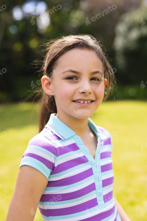 Preview: Vertical portrait of young caucasian girl wearing striped t-shirt and standing in the garden