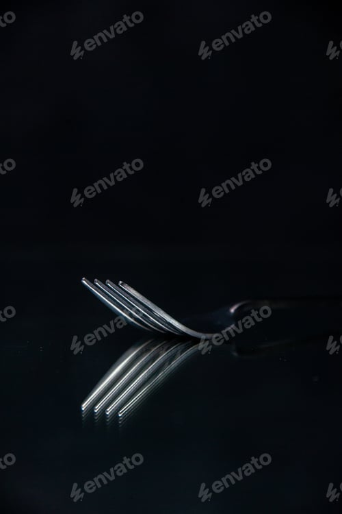 Preview: Half shot of elegant shiny metal fork on black wave background with free space in vertical view