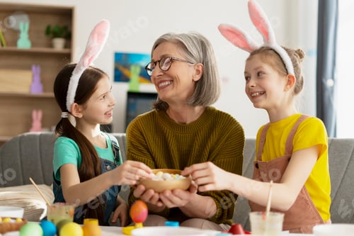 Preview: Grandmother sharing easter eggs with granddaughters wearing bunny ears