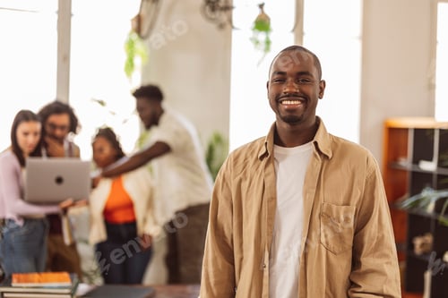 Preview: Portrait of a young African man office worker looking at camera, coworkers in background