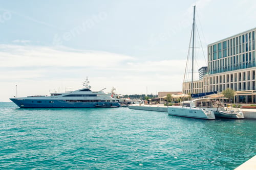 Preview: Luxury yachts moored at a marina with clear blue skies and modern architectural buildings