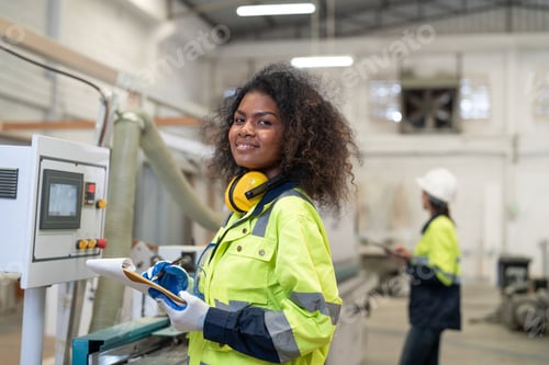 Preview: African American woman engineer operating CNC machine for cutting wood in furniture factory.