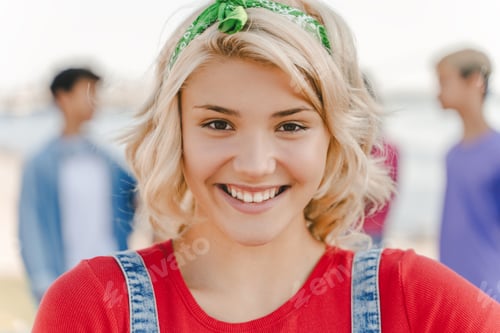 Preview: Smiling teenage girl wearing red t shirt looking at camera on the street with friends on background