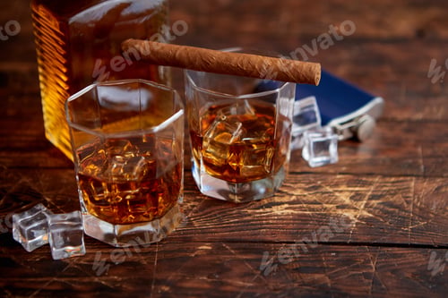Preview: Bottle of whiskey with two glasses and cuban cigar placed on rustic wooden table