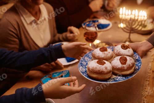 Preview: Close up of Jewish mother and daughter passing jam filled donuts during family meal on Hanukkah.