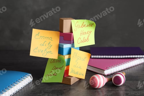 Preview: Paper notes with different baby names, toys and notebooks on grey table