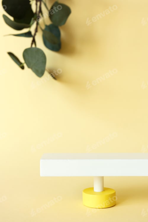 Preview: Abstract pedestal on pastel yellow background with copy space and defocused eucalyptus leaves