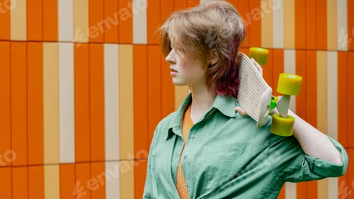Preview: Attractive skater young woman with skateboard against urban wall.
