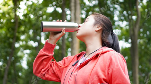 Preview: Asian women drinking water after exercise on green nature forest background