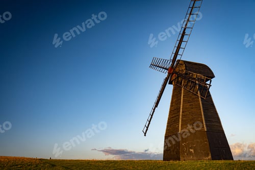 Preview: Low angle shot of a windmill in the middle of a field under the cloudy blue sky