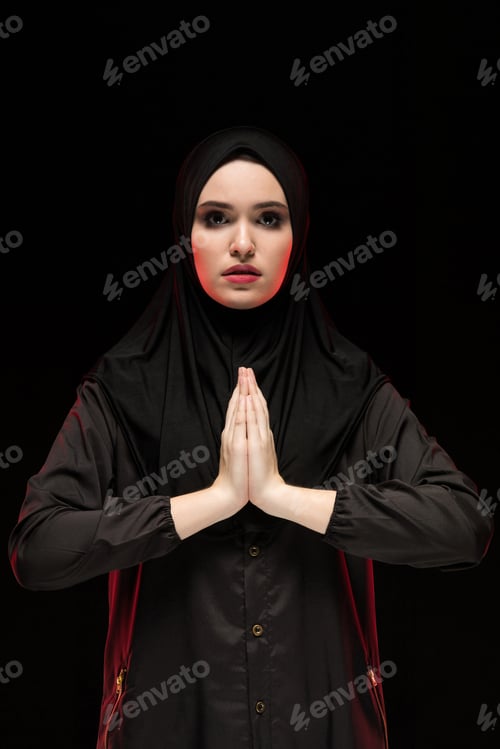Preview: Portrait of beautiful serious young muslim woman wearing black hijab with hands near her face as