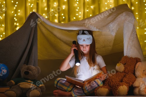 Preview: A pretty little girl reading a book on the floor under the lamp. Children and education.