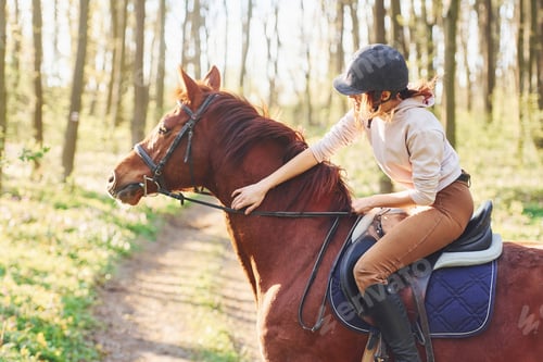 Preview: Young woman in protective hat with her horse in the forest at sunny daytime