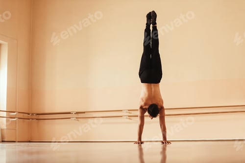 Preview: Rear view of male dancer doing handstand at dance studio.