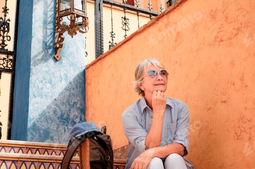 Preview: Smiling senior woman in leisure travel sitting on a staircase looking away.