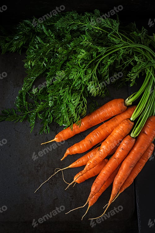 Preview: Bunch of fresh carrots with green leaves on dark background. Flat lay. Top view