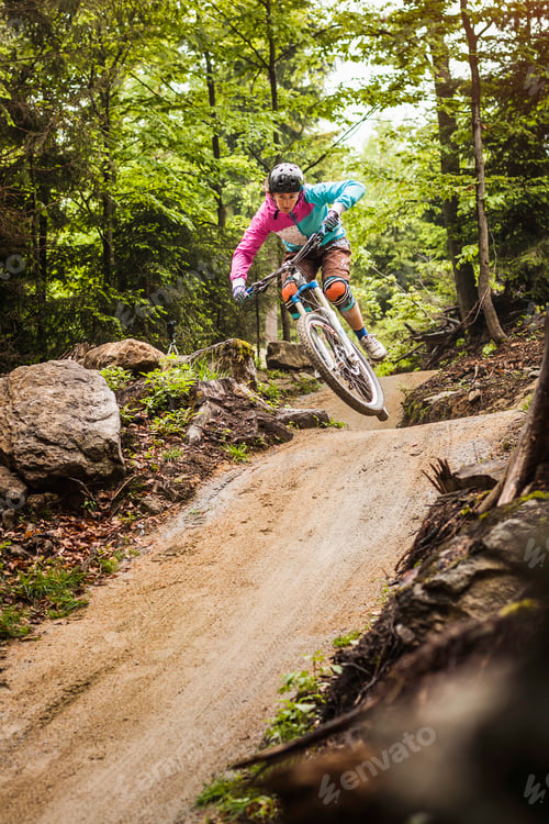 Preview: Young female mountain biker jumping mid air in forest