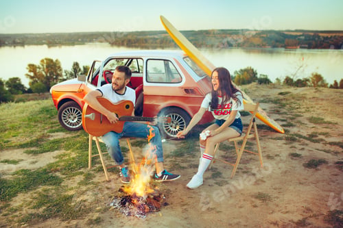 Preview: Couple sitting and resting on the beach playing guitar on a summer day near river