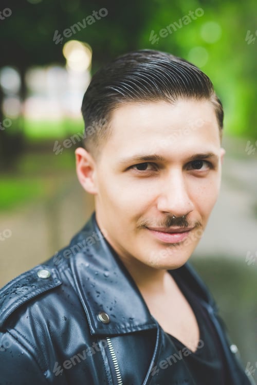 Preview: Stylish man with a slickedback haircut posing in a leather jacket outdoors.