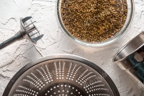 Preview: Bowl with cannabis seeds, a blender and a sieve on a white table