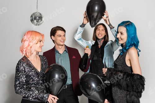 Preview: cheerful tattooed queer person holding black balloon above head near nonbinary friends talking on