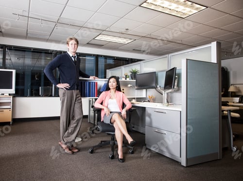 Preview: Caucasian businessman and Asian businesswoman team of people in a cubicle office space.