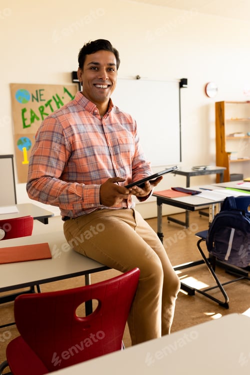 Preview: Portrait of happy biracial male teacher with tablet in elementary school classroom