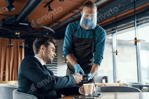 Preview: Handsome young businessman making a contactless payment while sitting in the restaurant
