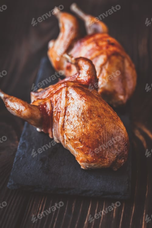 Preview: Two baked quails wrapped in bacon on the black stone board