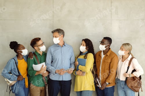 Preview: Group of university students and their professor wearing face masks while talking against wall.