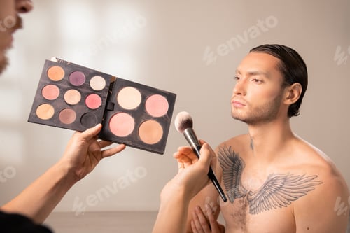 Preview: Hands of young makeup artist holding eye shadow palette and brush