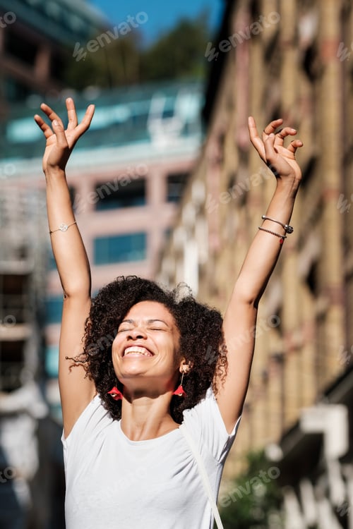 Preview: Happy black woman with arms up in the street.