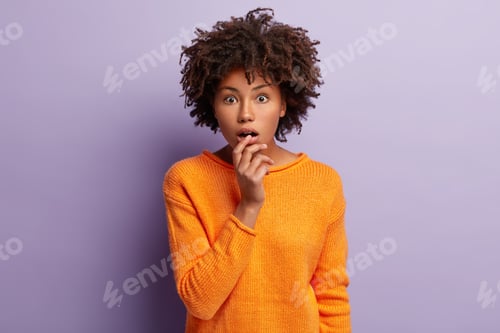 Preview: Dazed young curly female looks at camera with fright, keeps widely opened eyes and mouth, can not be