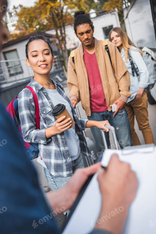 Preview: partial view of bus controller writing in clipboard while multiethnic tourists standing near travel