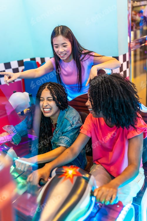 Preview: Young women playing arcade game together in amusement park
