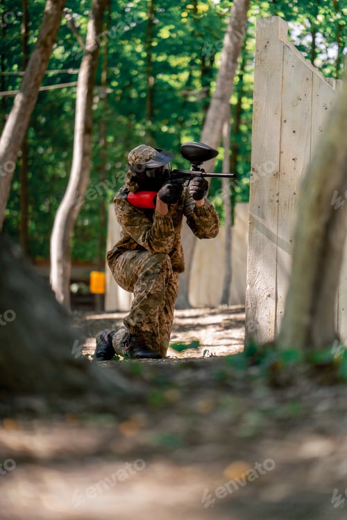 Preview: in the wild near tree structures player in a pintball uniform holds a pistol with a red balloon team