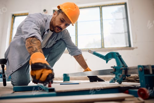 Preview: Manual worker cutting ceramic tiles during floor installation at renovation home.