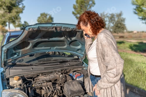 Preview: Senior Woman making a call for roadside assistance with her car hood open