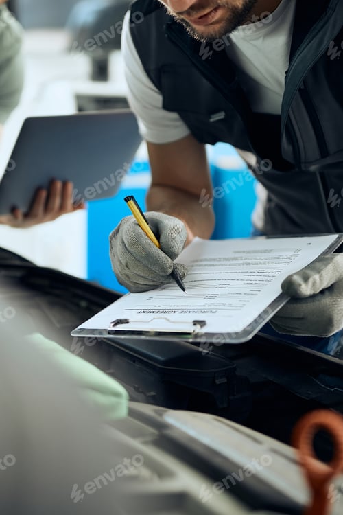 Preview: Close up of mechanic taking notes while analyzing car engine with his coworker in a workshop.