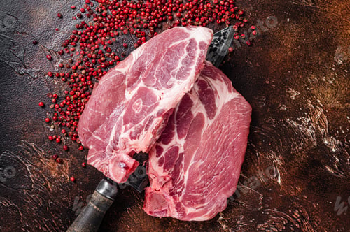 Preview: Pork loin steak from raw neck fillet meat on butcher knife. Dark background. Top view