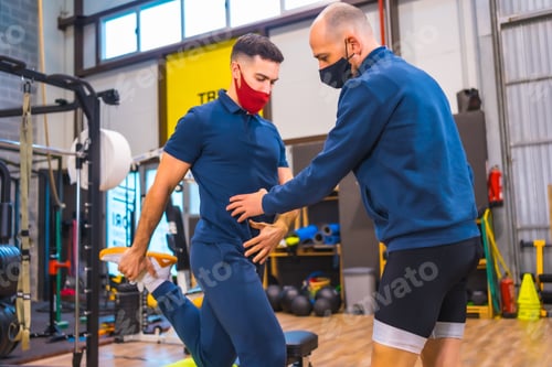 Preview: Young athlete with an instructor in gym doing exercises with strips in the coronavirus pandemic