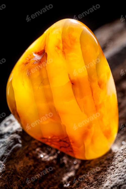 Preview: Natural amber. A piece of yellow opaque natural amber on large piece of dark stoned wood