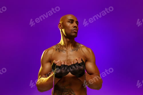 Preview: Man with athletic body performs exercises using resistance band on studio background