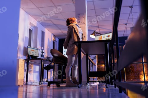 Preview: Tired entrepreneur standing up and streching neck after working overhours
