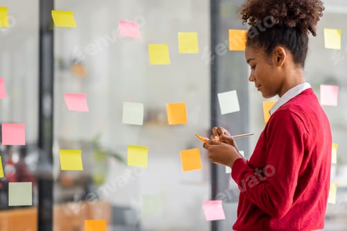 Preview: Young mixed african american businesswoman with afro hairstyle planning on whiteboard in a startup