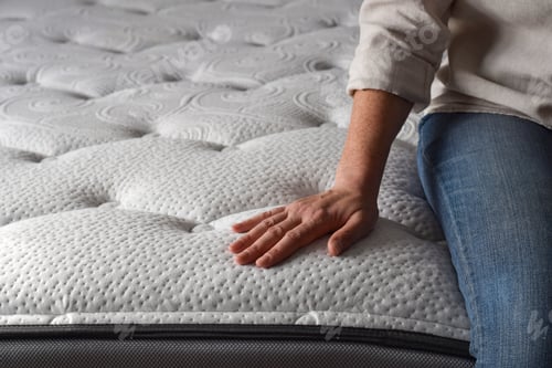 Preview: Woman sitting on a brand new mattress and touching the fabric
