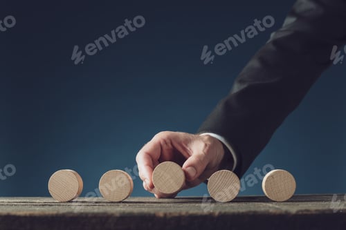 Preview: Hand of a businessman placing five blank wooden cut circles in a row